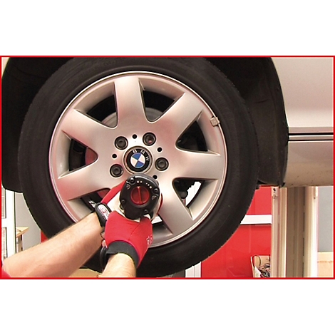 Ein Mann verschraubt mit einem Schlagschrauber ein Rad an einem BMW. Der Reifen und die Felge sind silberfarben. Der Mann trägt rote Handschuhe.